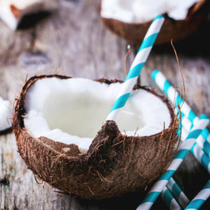 Broken coconut with coconut milk and vintage cocktail tubes on old wooden table. Square image